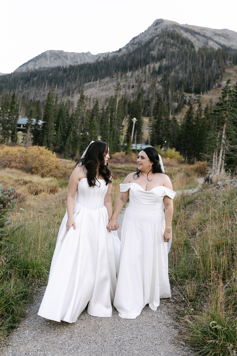 Two brides stand together on paved path, their Knoxville wedding venue in the background.