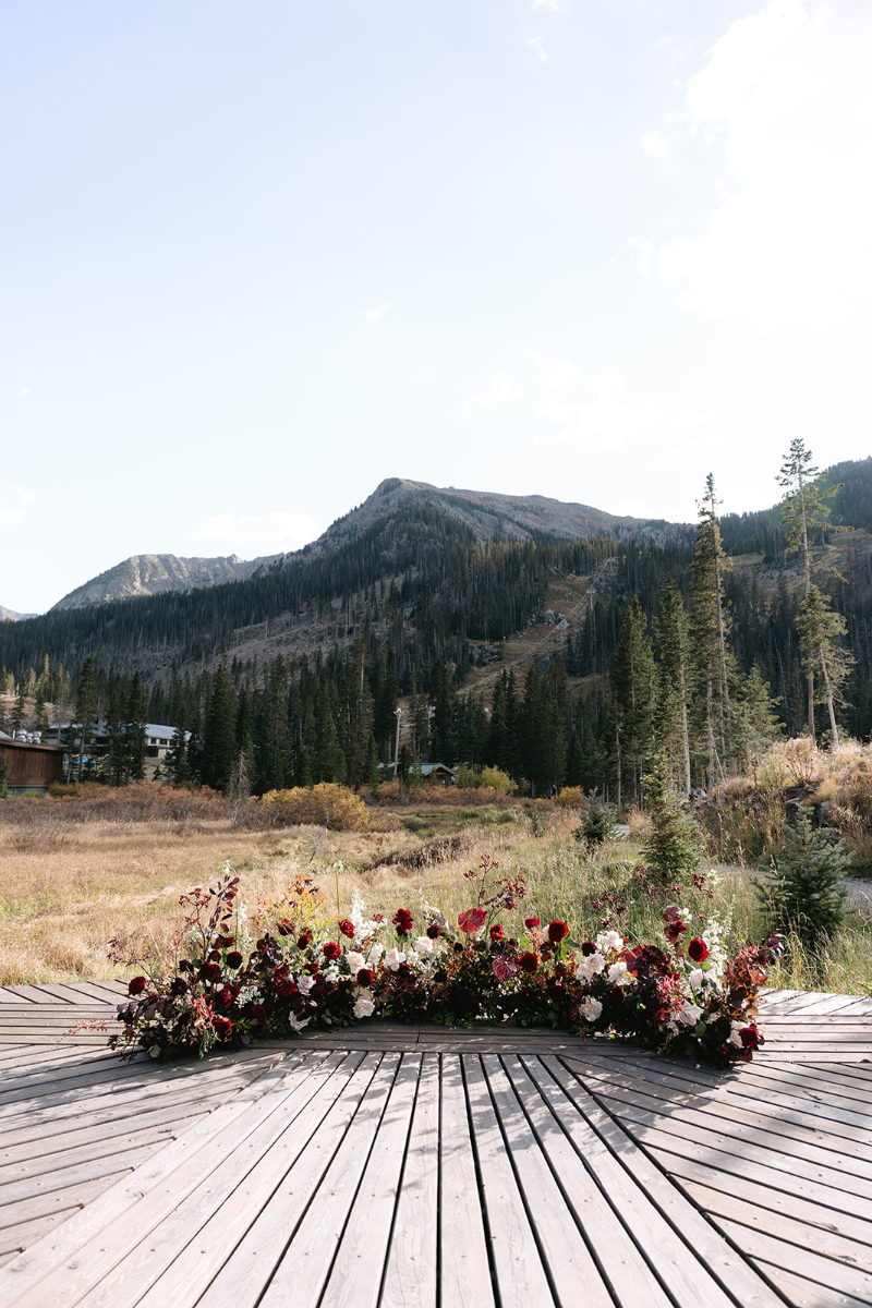 Floral meadow in shades of red placed on wooden structure for wedding ceremony with a mountain backdrop, one shared by many Knoxville wedding venues.