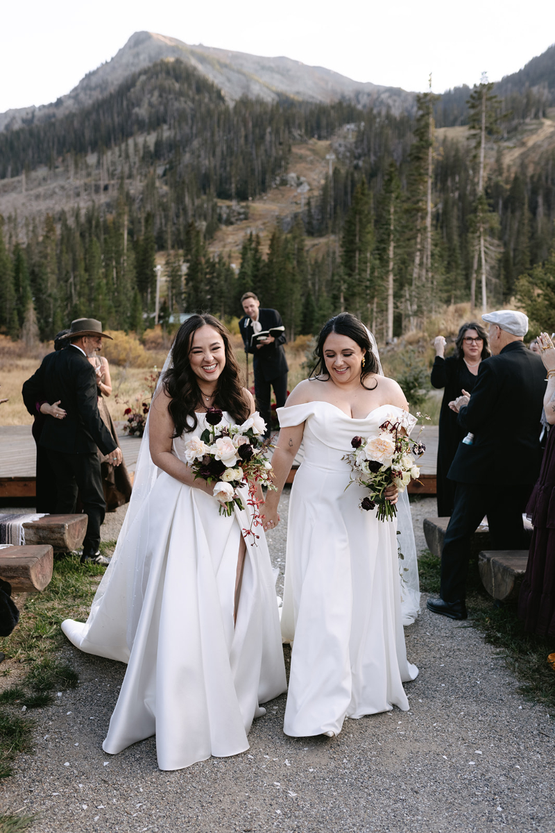 Brides process aisle after just exchanging vows during their wedding ceremony in the mountains.