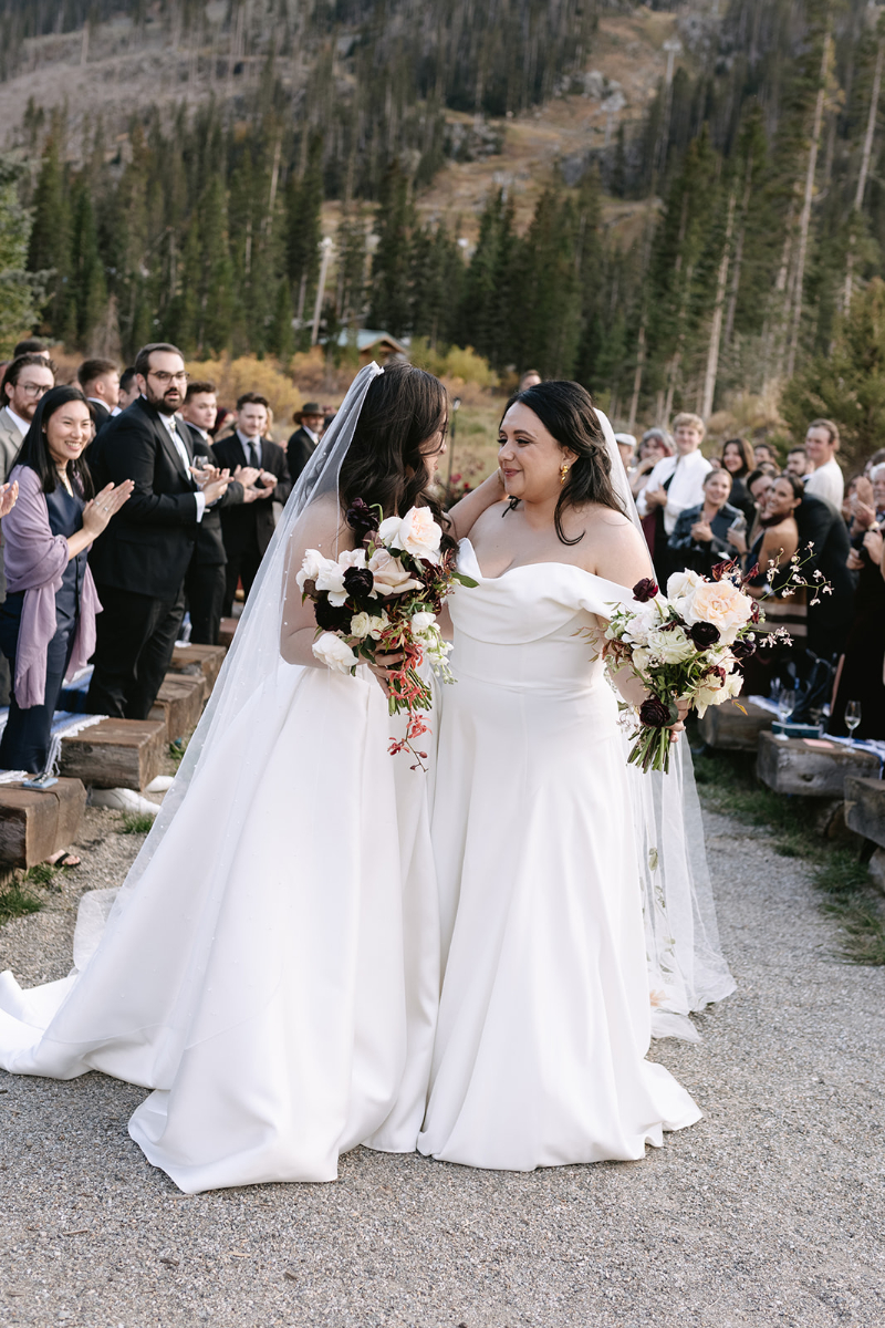 Brides process aisle after just exchanging vows during their wedding ceremony in the mountains.
