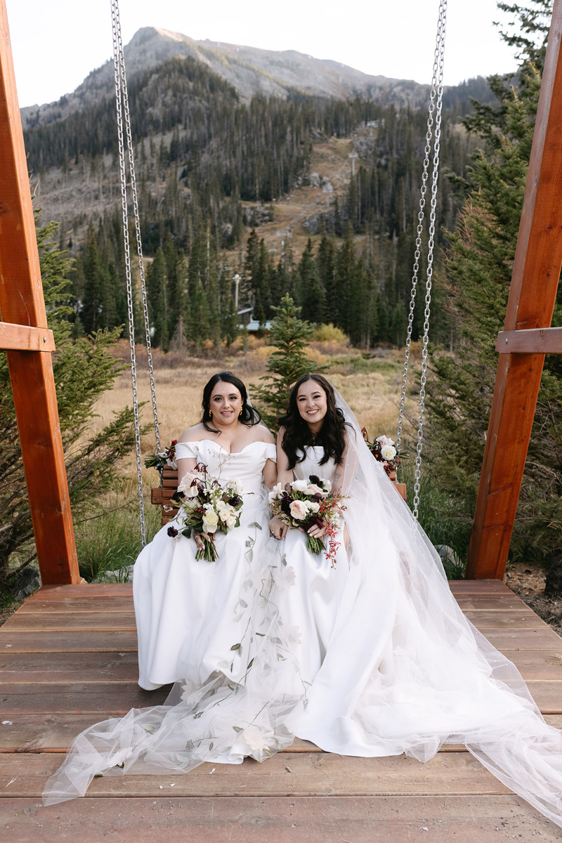 Two brides sit together in swing after exchanging vows at their wedding.