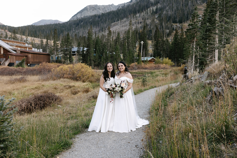 Two brides stand together on paved path, their Knoxville wedding venue in the background.