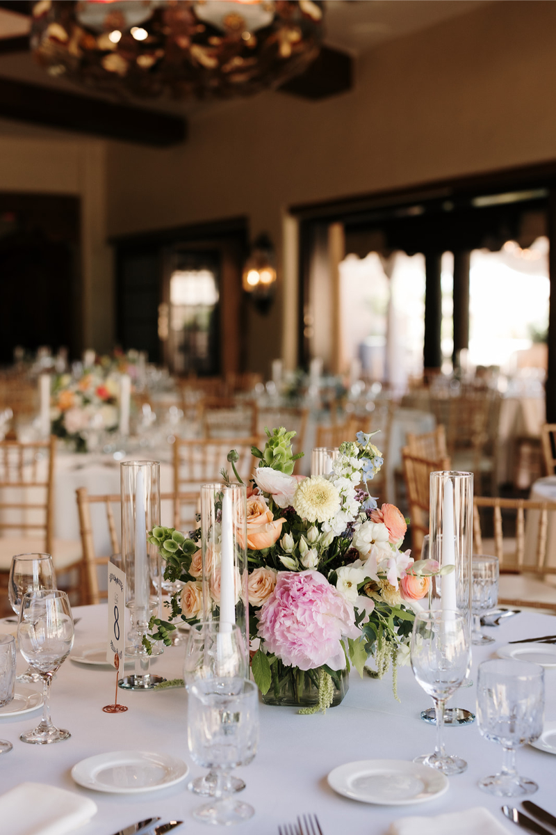 Low floral centerpiece surrounded by pillar candles in glass hurricanes.