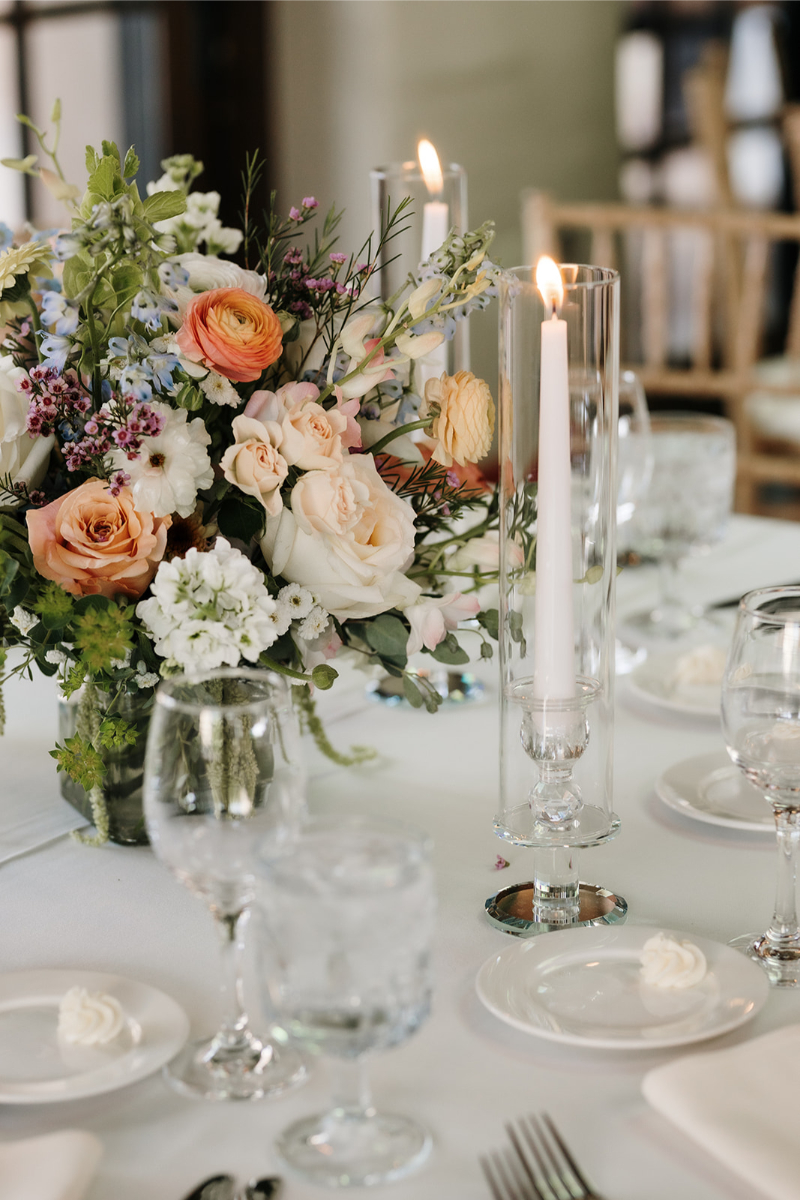 Low floral centerpiece surrounded by pillar candles in glass hurricanes.