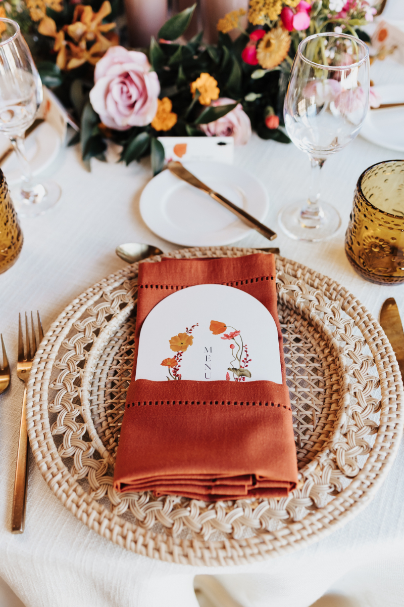 Place setting with rattan charger, terracotta napkin with menu folded into it.