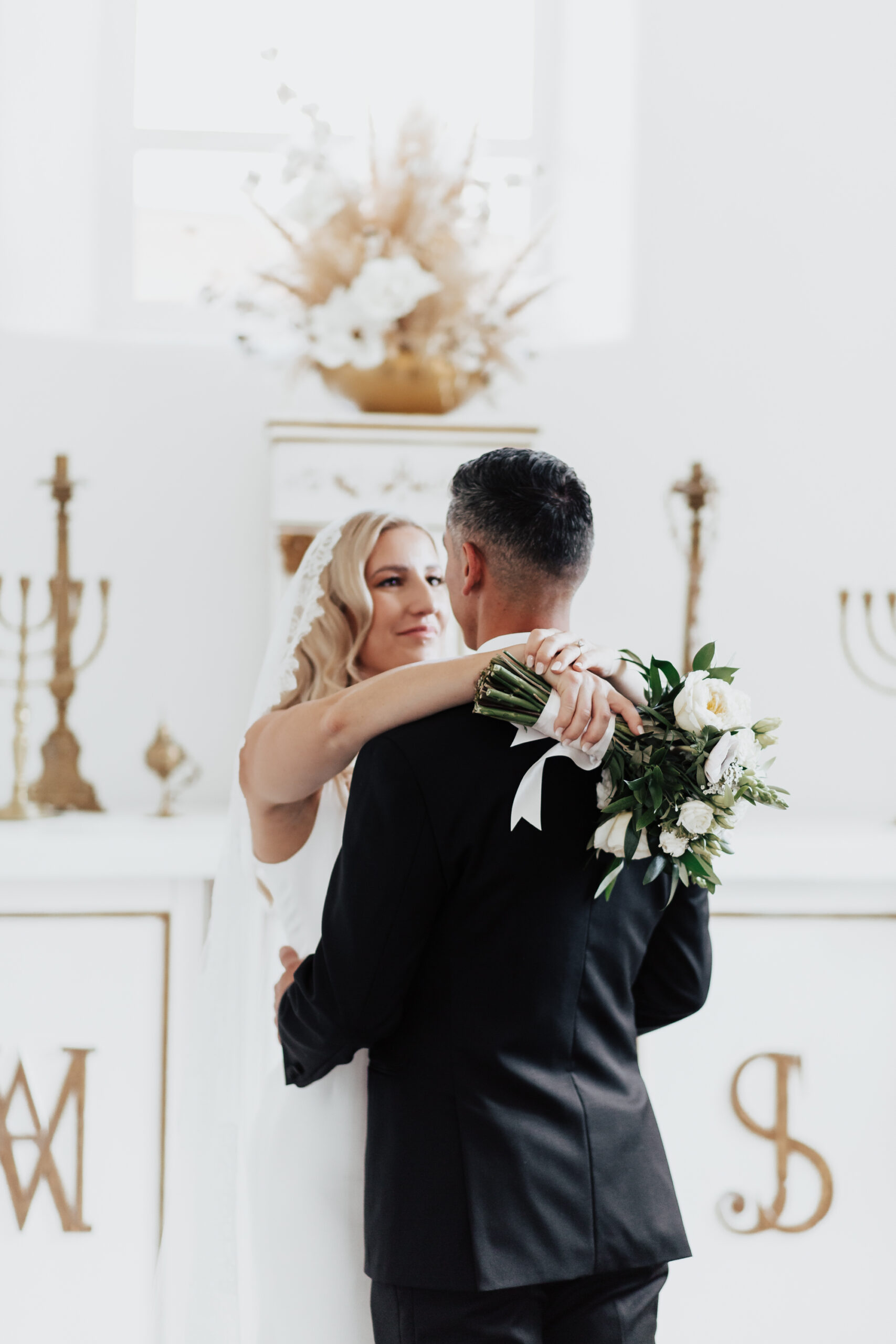 Bride wraps her hand around groom's neck as she holds white bouquet in her hand.