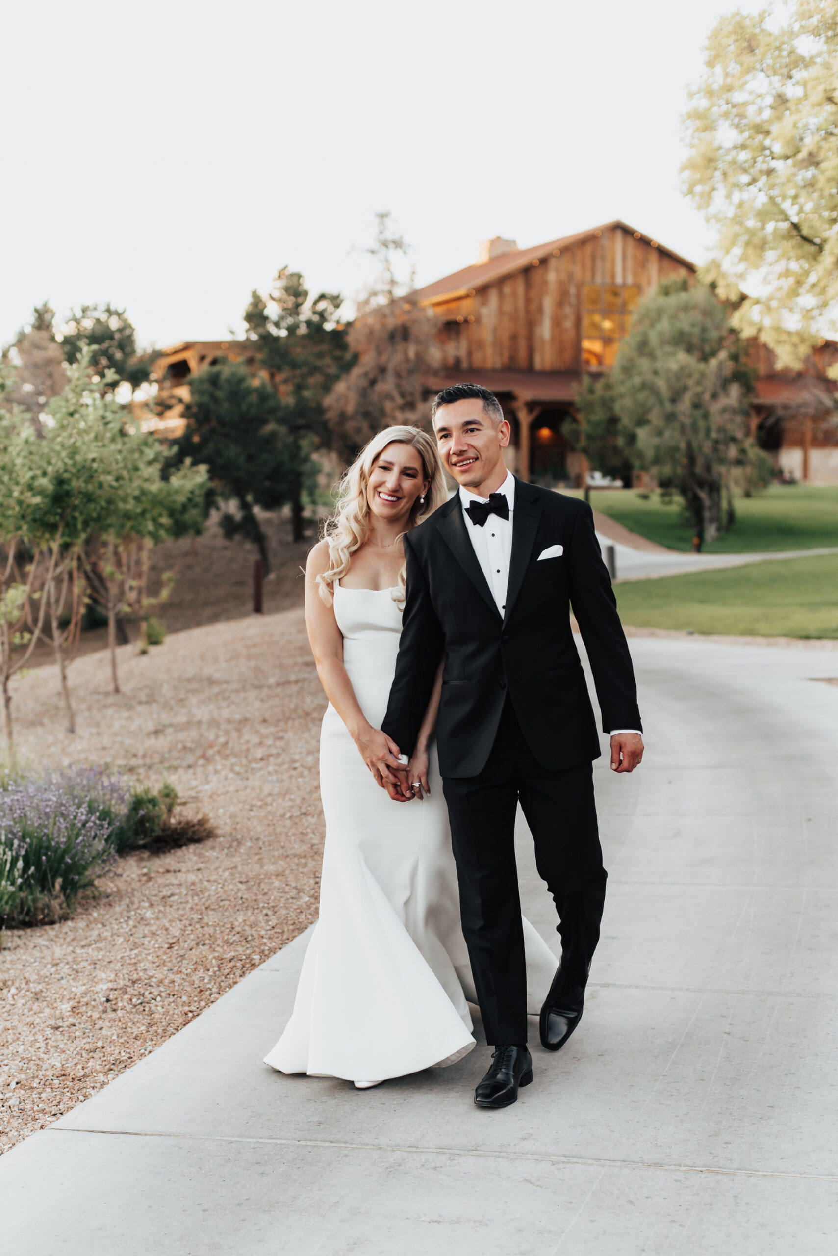 Bride and groom walk hand in hand along sidewalk with their venue for their wedding in Tennessee behind them.