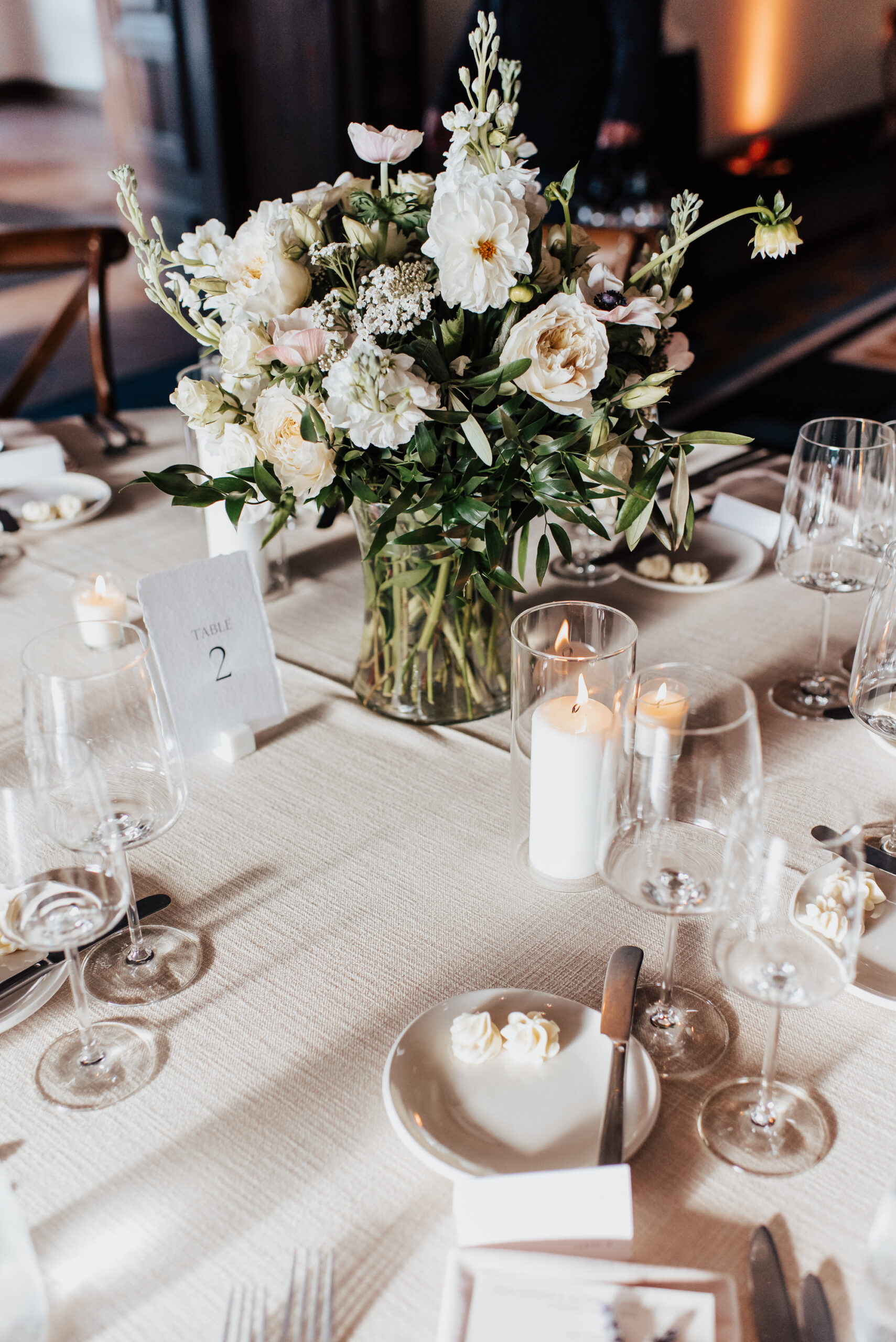 Tablescape decorated with white linens, low white floral arrangement, and gold flatware.
