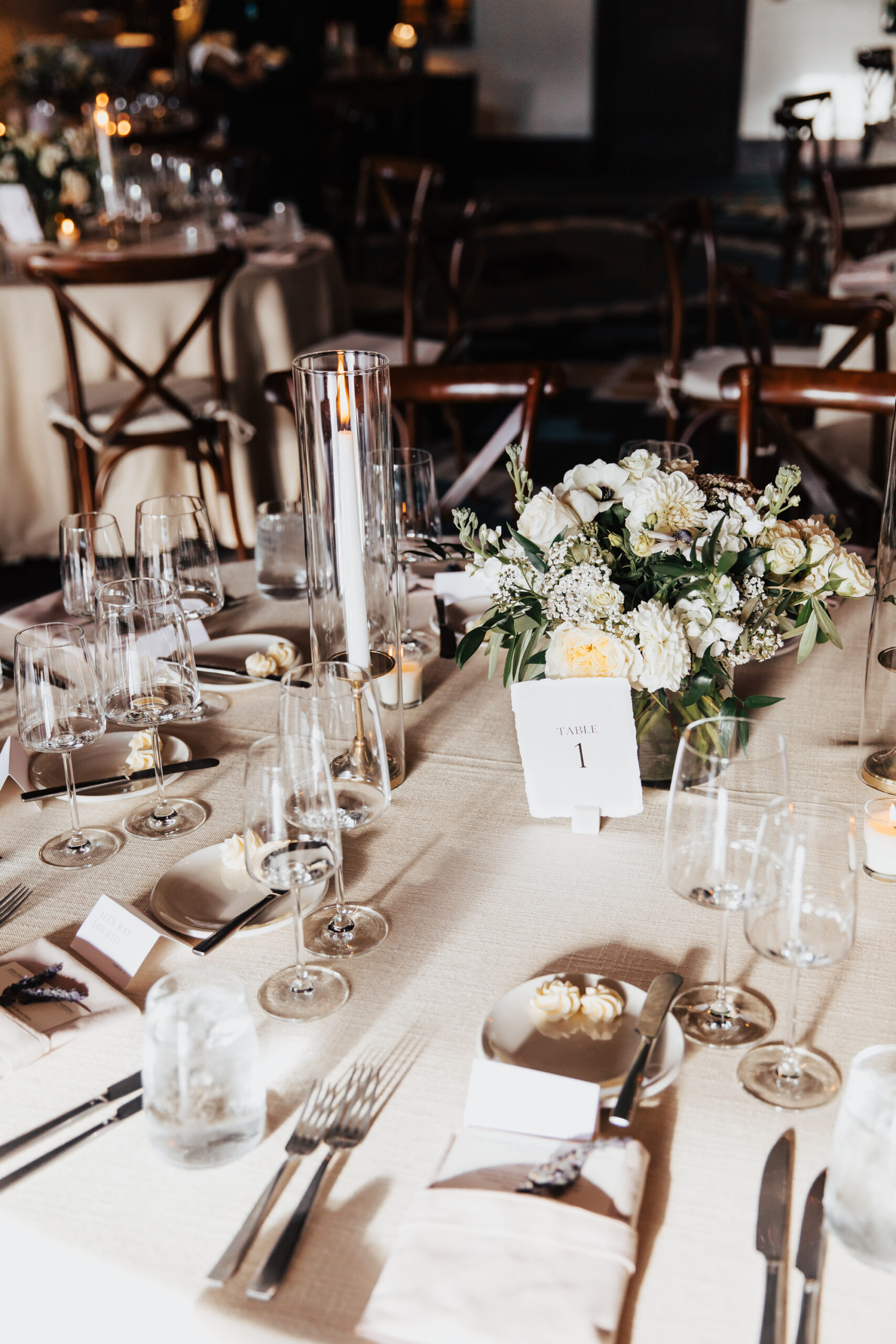 Tablescape decorated with white linens, low white floral arrangement, and gold flatware.