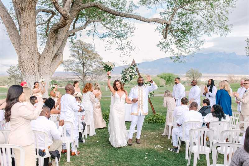 Bride and groom throw their hands in the air as they are celebrated when exiting their ceremony - guests happy they answered the question "what time do weddings start" when choosing their New Mexico ceremony time.