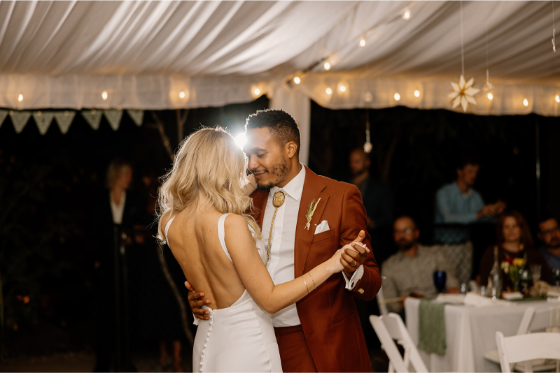 Bride and groom share first dance under tented reception with string lights glowing above them.