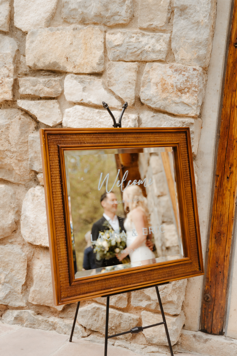 Bride and groom stand together in front of mirror welcome sign.