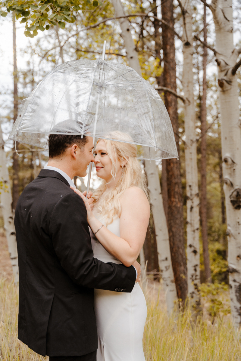 Bride and groom stand together under a clear umbrella for their bridal portraits at their outdoor wedding venues in New Mexico.