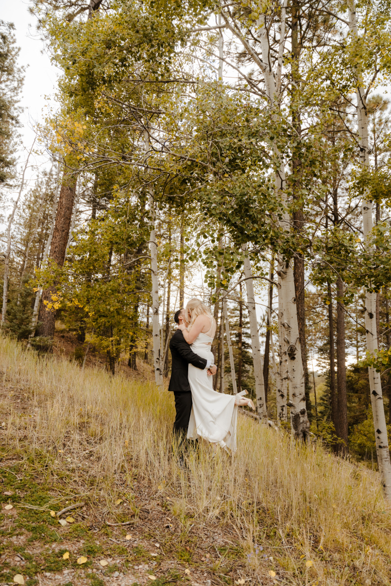 Groom lifts up bride as they kiss during wedding portraits.