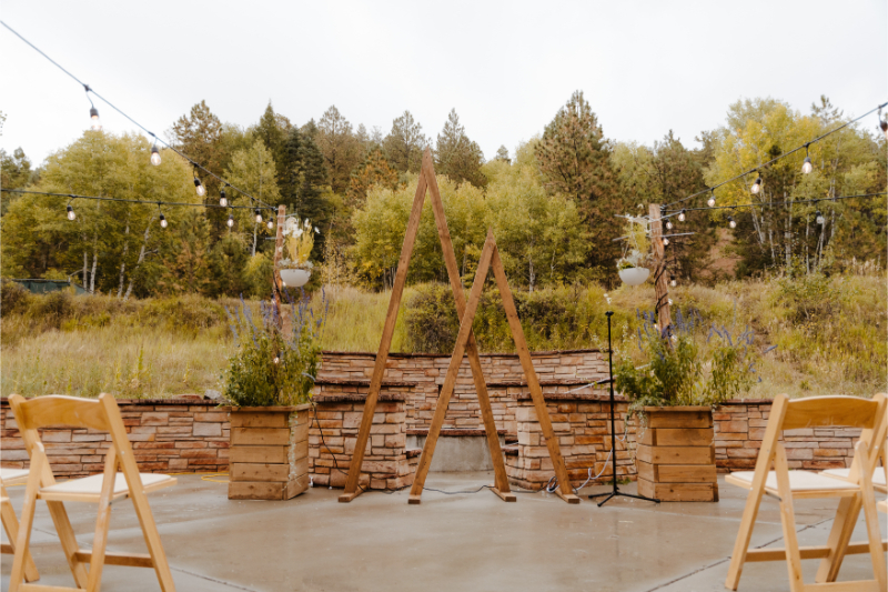 Outdoor wedding venues in New Mexico set up for ceremony with string lights, wood triangle arch, and wooden folding chairs.