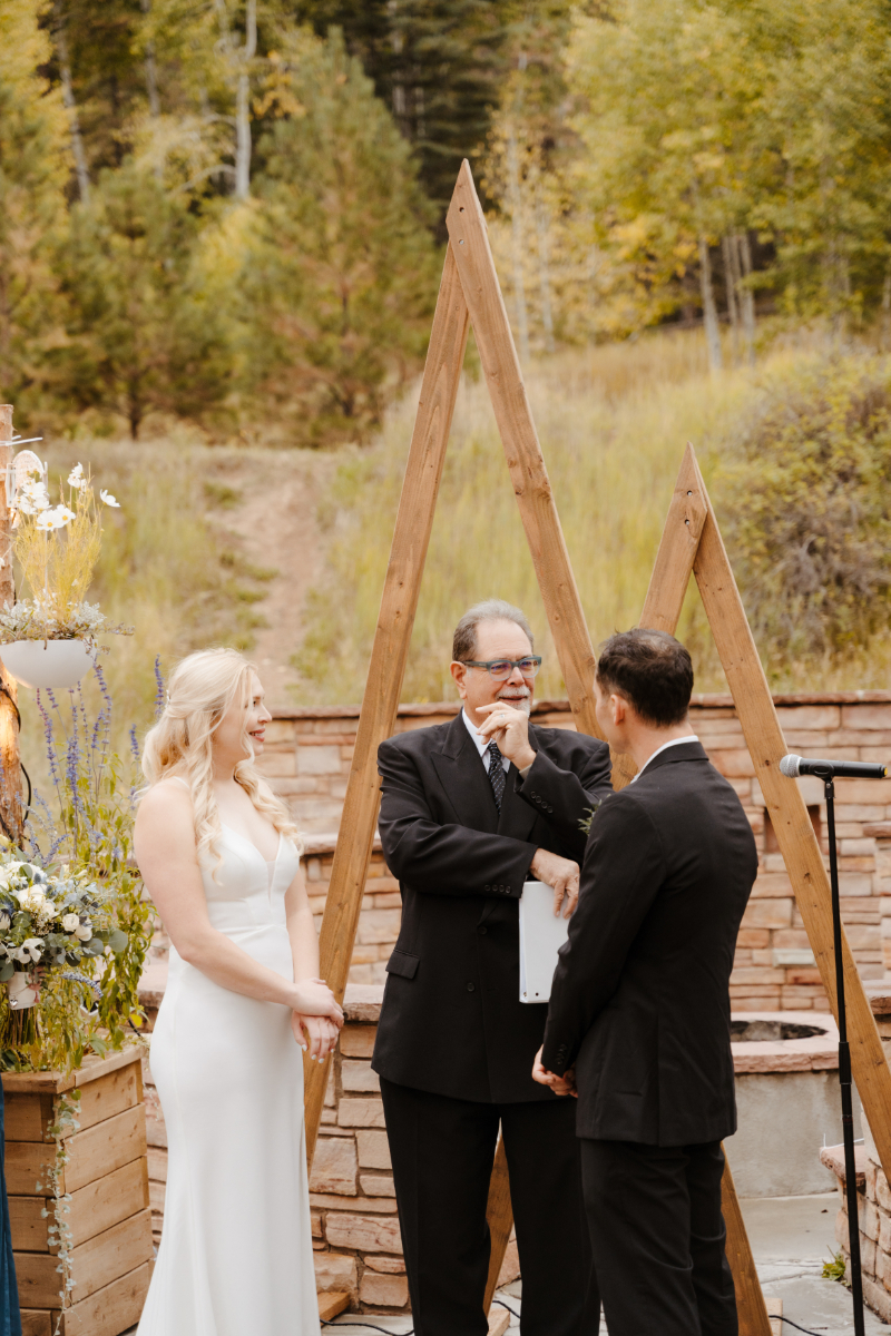 Bride and groom stand at altar with a wooden triangle arch set behind them.