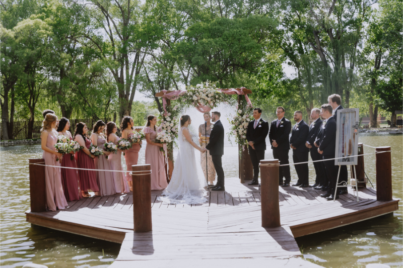 Bride and groom hold hands as they exchange vows while standing on a dock in the middle of a Nashville wedding venues on-site pond.