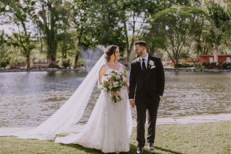 Bride and groom walk hand in hand on lawn with a pond behind them on their Nashville wedding venues property.