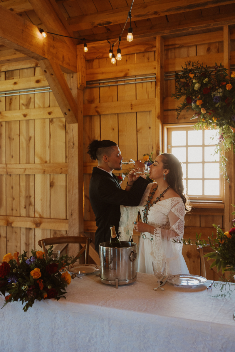 Bride and groom interlace their arms as they both drink champagne before cutting the cake.