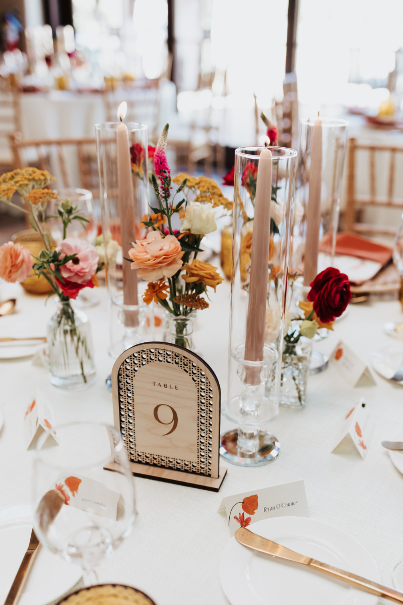 Bud vases with colorful wildflowers arranged next to pillar candles in glass hurricanes.