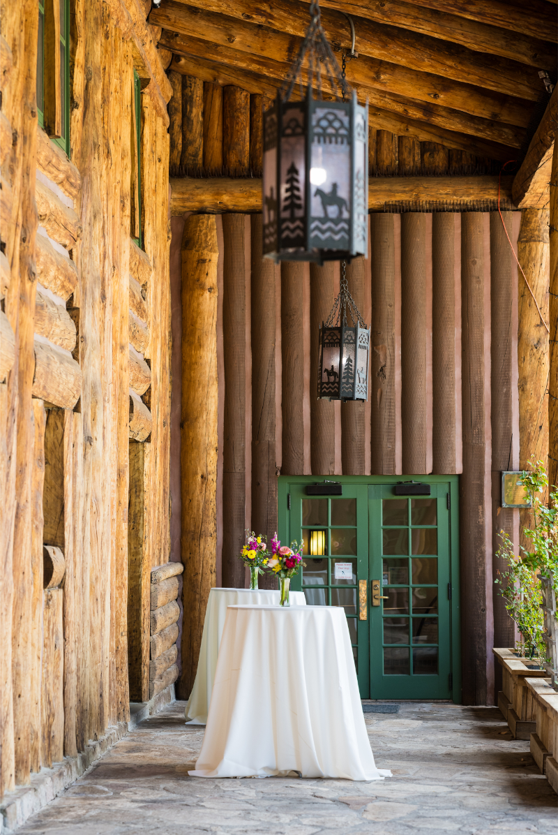 Bar table draped with white linen and a green vase with wildflowers spilling out.