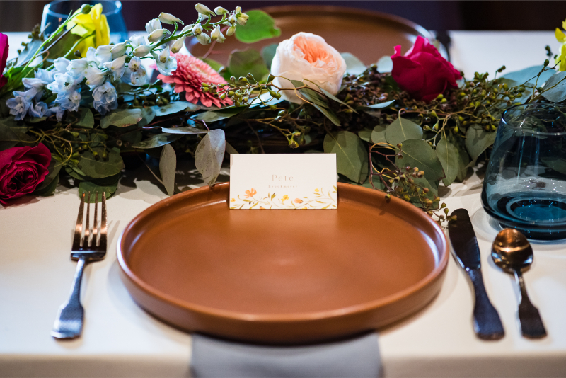 Table setting with gold cutlery and low floral arrangement.