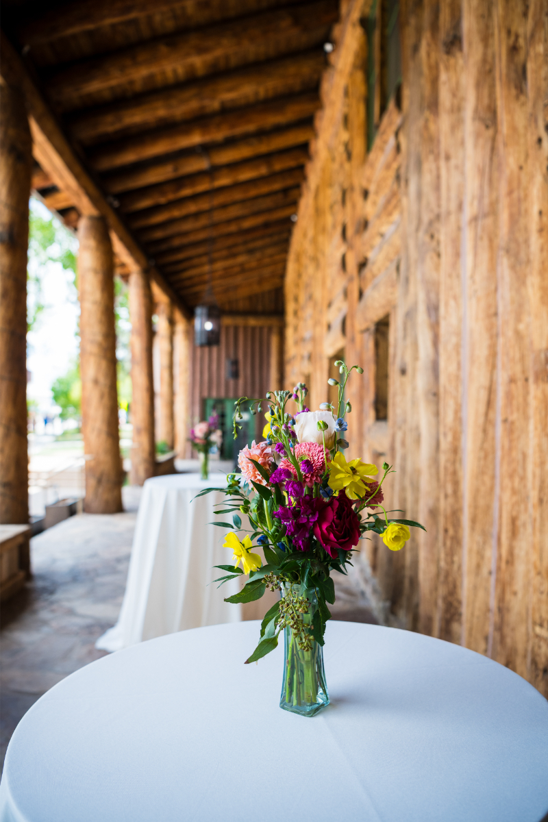 A green vase with wildflowers sitting on white table cloth covering bar height table at wedding reception in New Mexico.