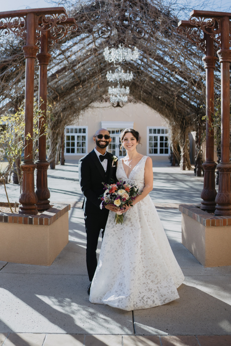 Bride and groom take wedding portraits underneath an arbor during their desert botanical garden wedding.