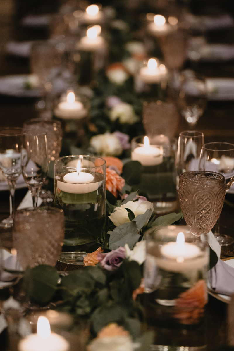 Close up view of tablescape set down a long rectangle table, with candles floating in water and greenery.
