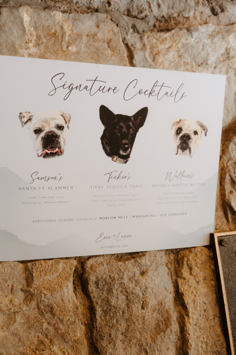 A signature cocktail menu board for a new mexico micro wedding featuring illustrated watercolor portraits of the couple's three dogs, each paired with a named cocktail. Samson's Santa Fe Slammer, Tinker's Tipsy Tequila Tonic, and Wallace's Whiskey Whistle Wetter are listed alongside additional classic cocktails, against a soft mountain silhouette background.