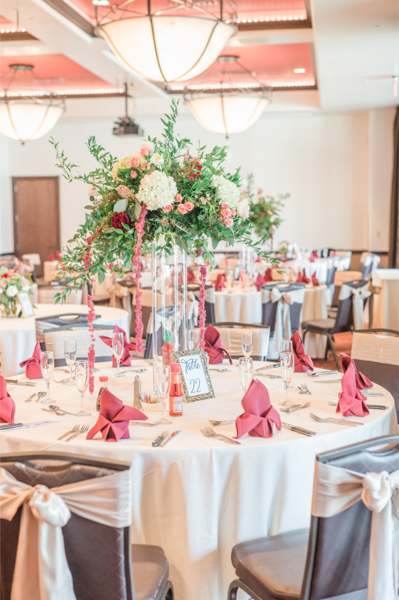 Tall flower arrangements of white hydrangea, blush roses, and trailing amaranthus in clear glass vases on round banquet tables.
