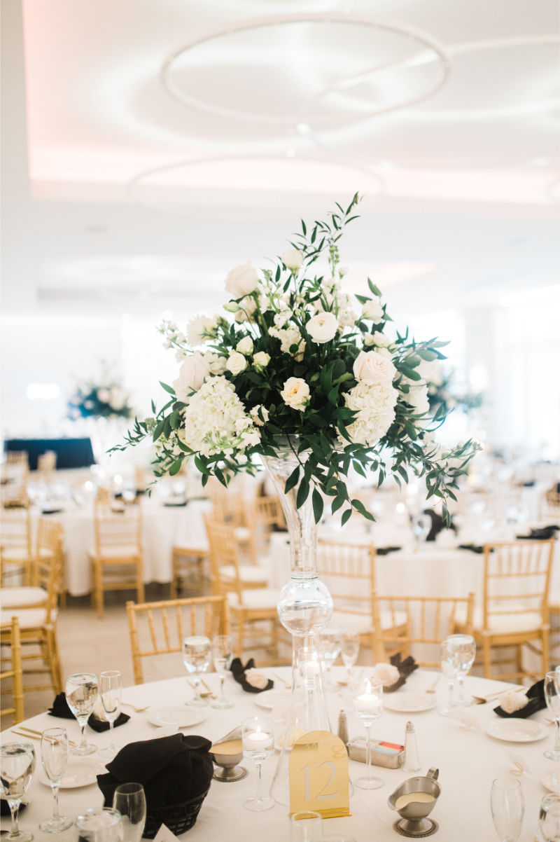 Lush white and green centerpiece arrangement with garden roses, hydrangea, and sprawling eucalyptus in a tall fluted glass vase.