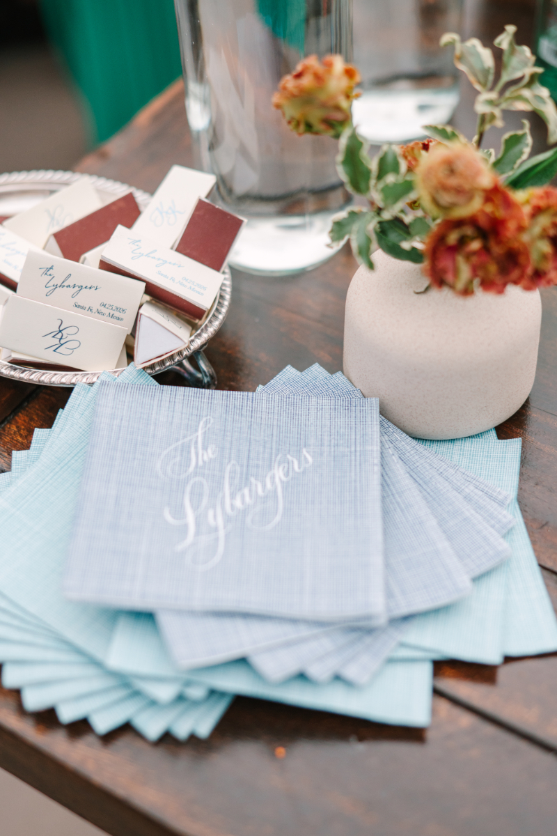 Personalized blue cocktail napkins and custom matchbooks with small terracotta floral arrangement at a Tennessee wedding venues bar station.