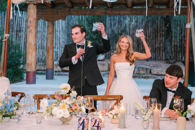 Bride and groom raising a toast at their Tennessee wedding venues reception under a sailcloth tent with rustic log posts and colorful floral centerpieces.
