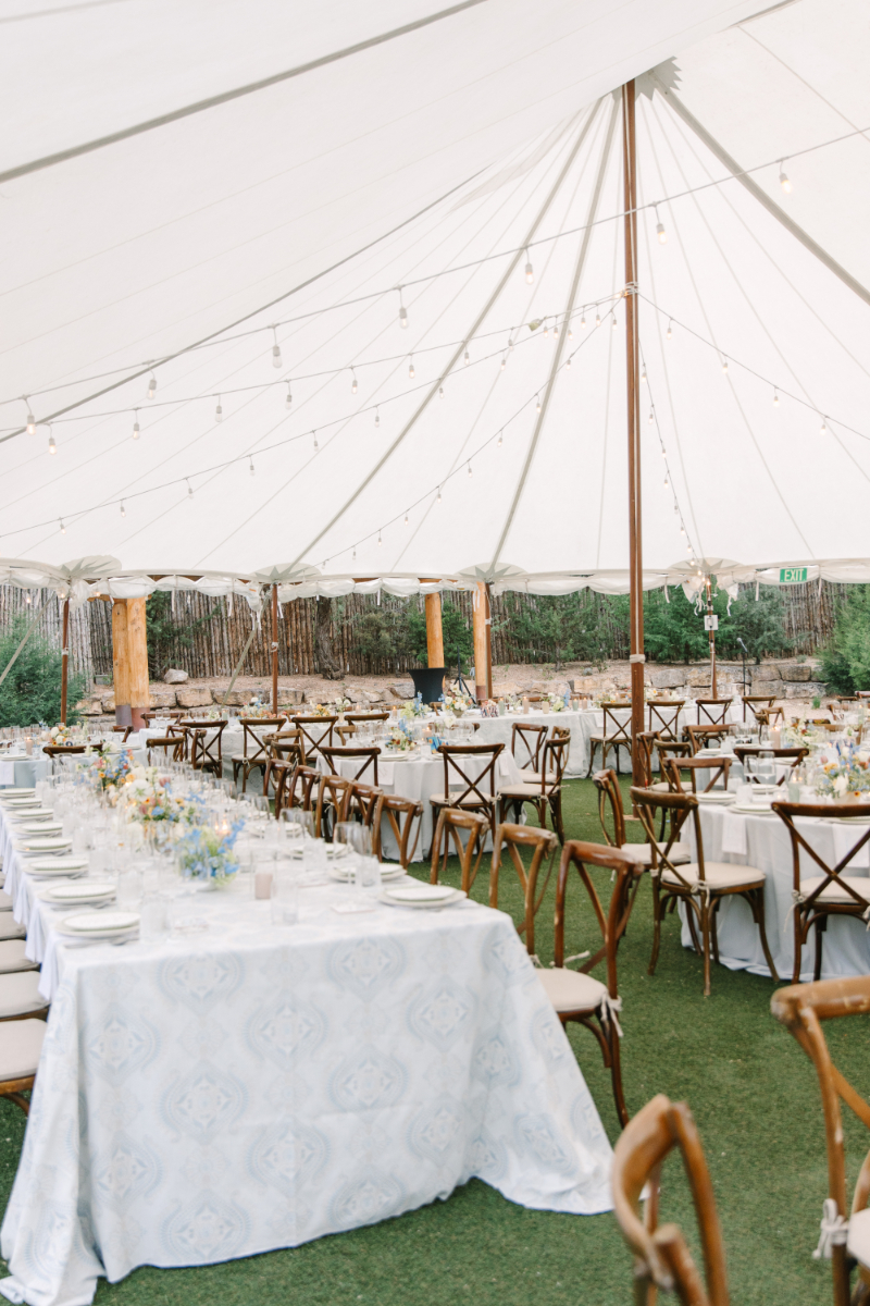 Sailcloth tent reception at Tennessee wedding venues with patterned blue linens, crossback chairs, and string lights overhead.