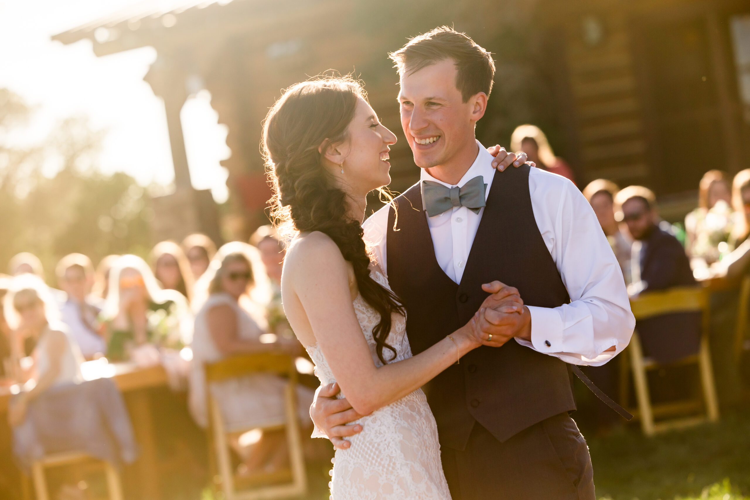 Bride and groom share first dance with the golden hour sun flaring in the corner of the photo behind them.