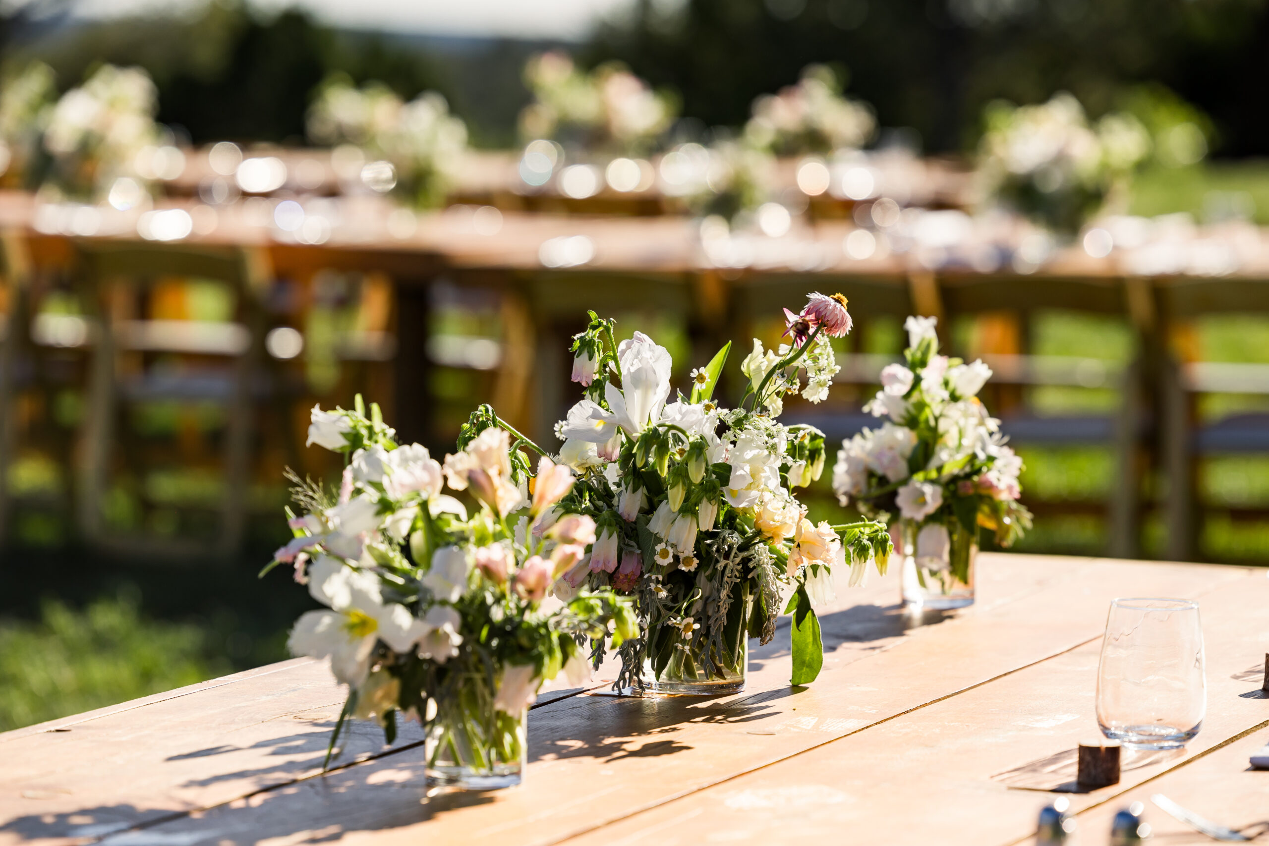 Three wildflower wedding centerpieces sit on reception table for country wedding.