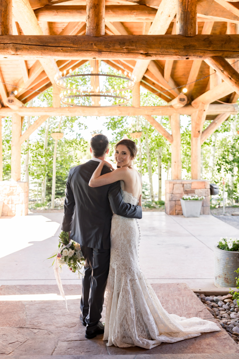 Bride looks over grooms shoulder as they take portraits underneath a beautiful light barn, which perfectly executed all of their elevated country wedding ideas.