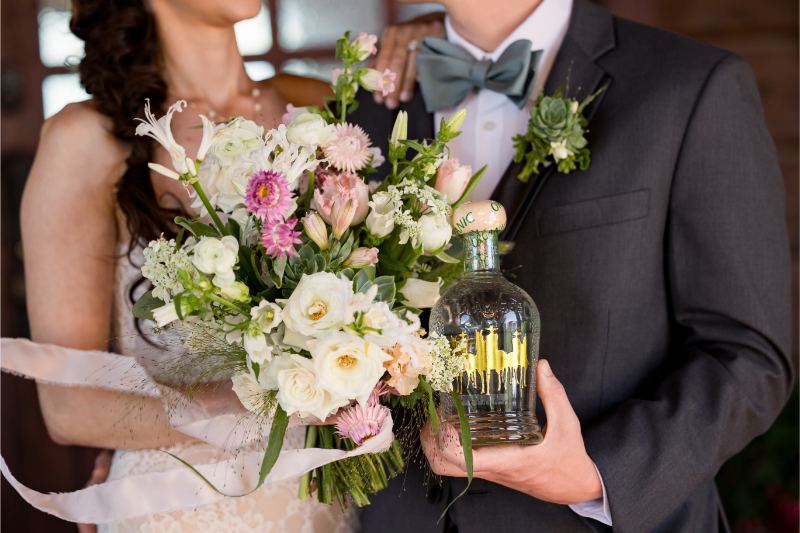 Close up of bride and groom holding bouquet and bottle during their portraits.