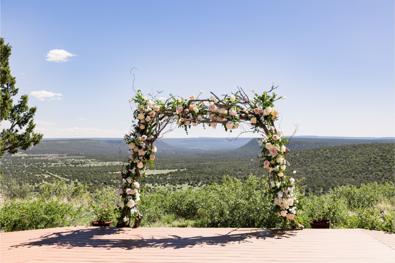 Square floral arch sits above a mountaintop overlooking rolling hills.