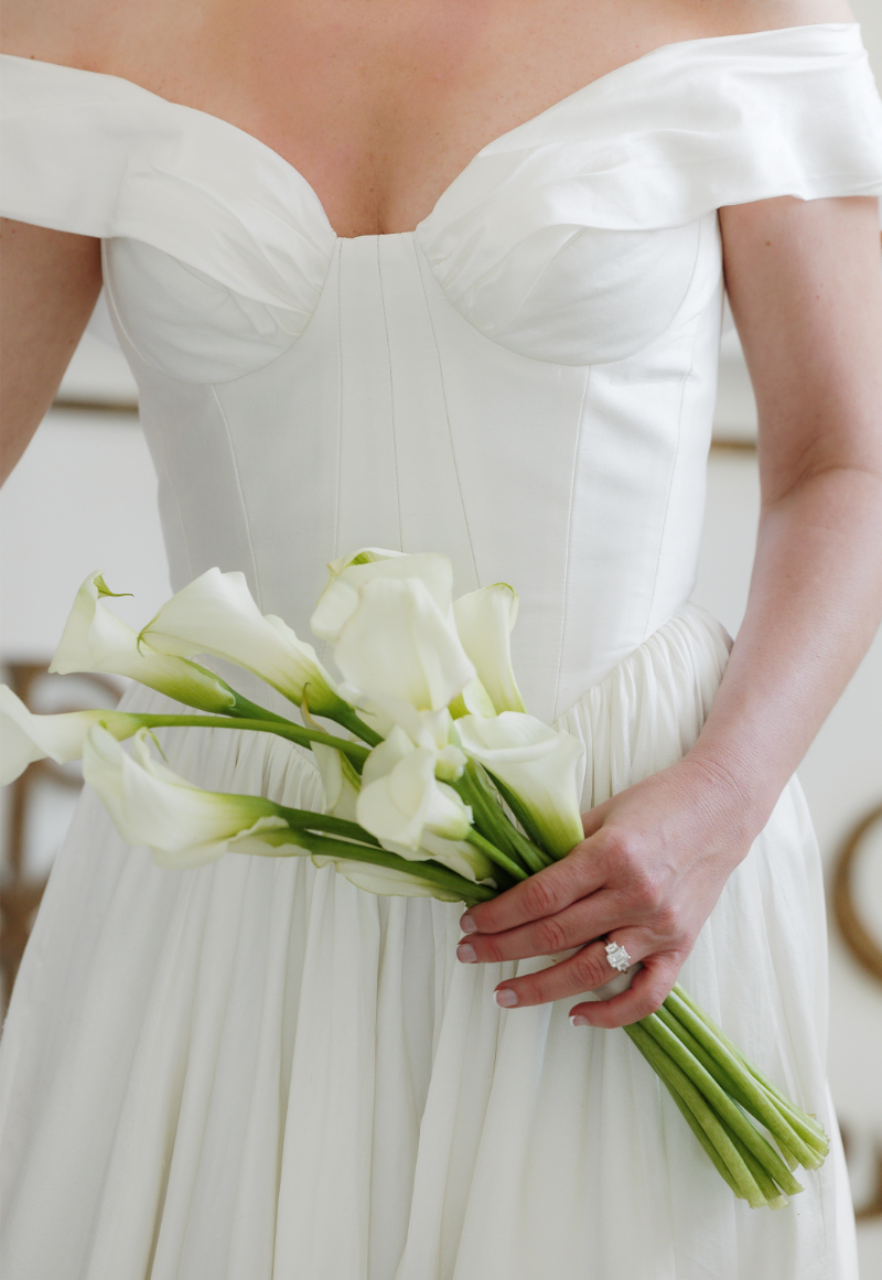 Bride holds bouquet of calla lily stems.