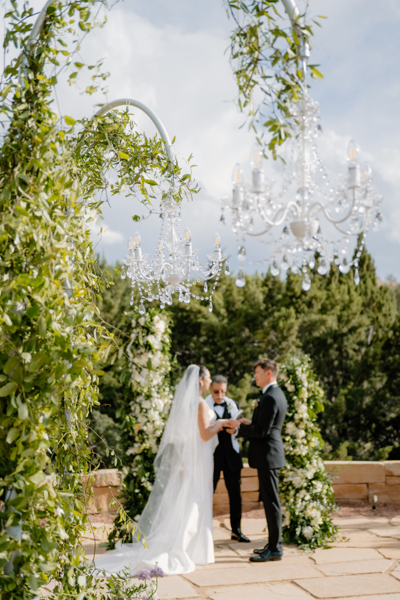 Bride and groom exchange vows under a unique arched floral arrangement, one of the brides wedding arch ideas she wanted to execute.