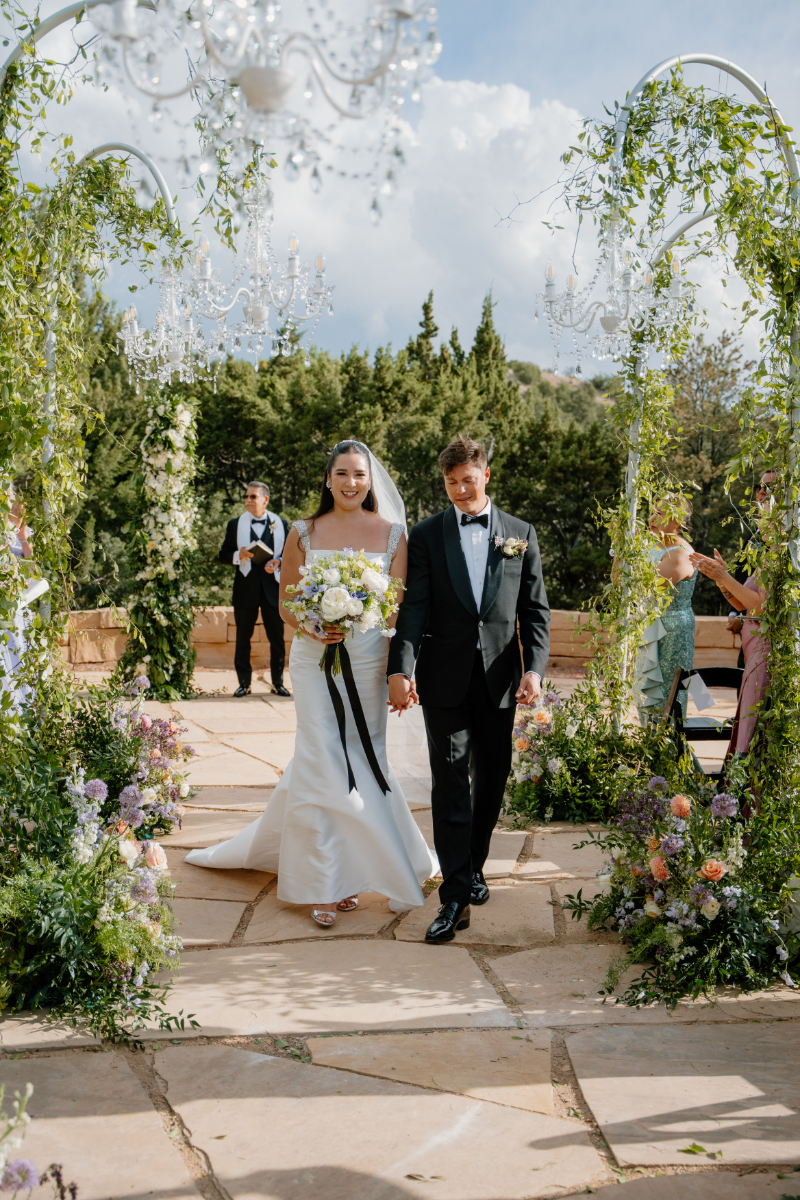 Bride and groom walk hand in hand down the aisle.