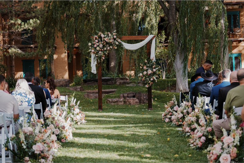 Guests sit in white folding chairs looking at the wedding arch ideas brought to life by the designer and florist.