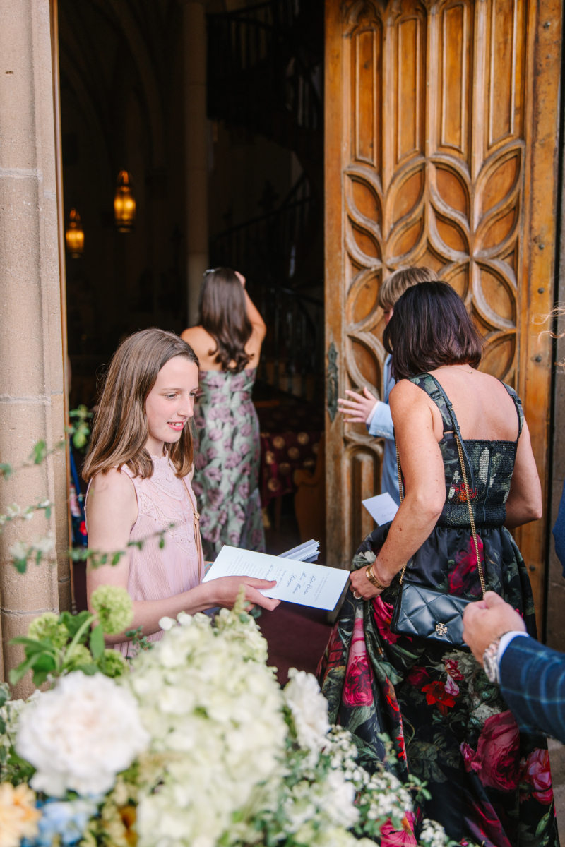 Girl hands out wedding ceremony stationery as guest enter church.