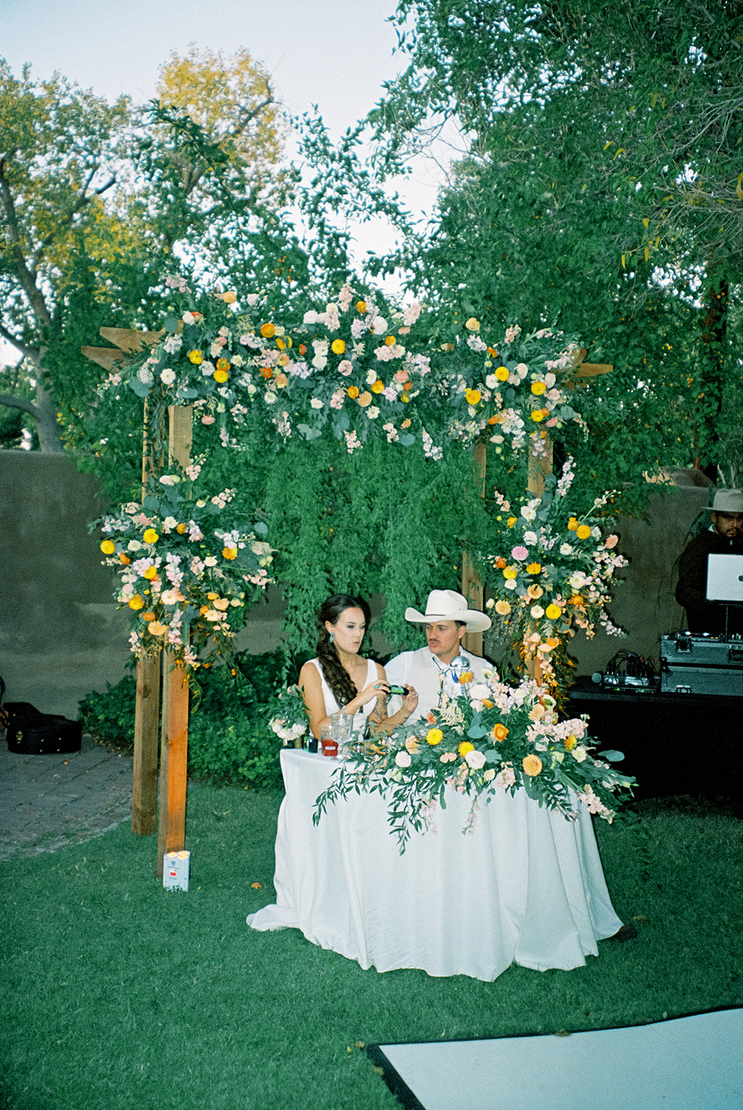Bride and groom sit at sweet heart table, surrounded by a wildflower arrangement.