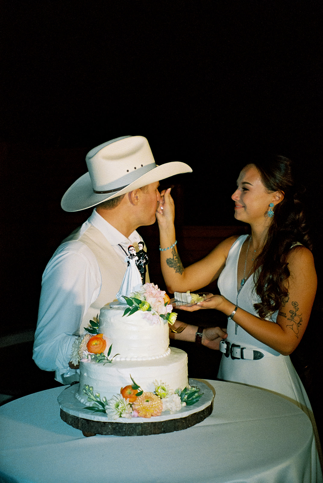 Bride feeds groom a bite of cake during their cake cutting at a western wedding reception.