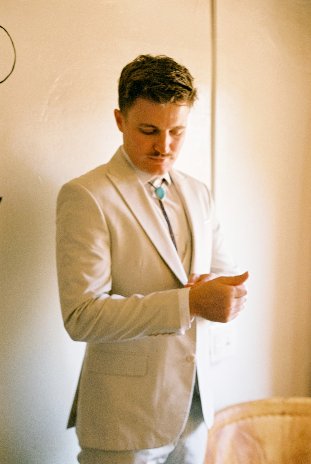 Groom wearing a tan suit buttons his cuff links.