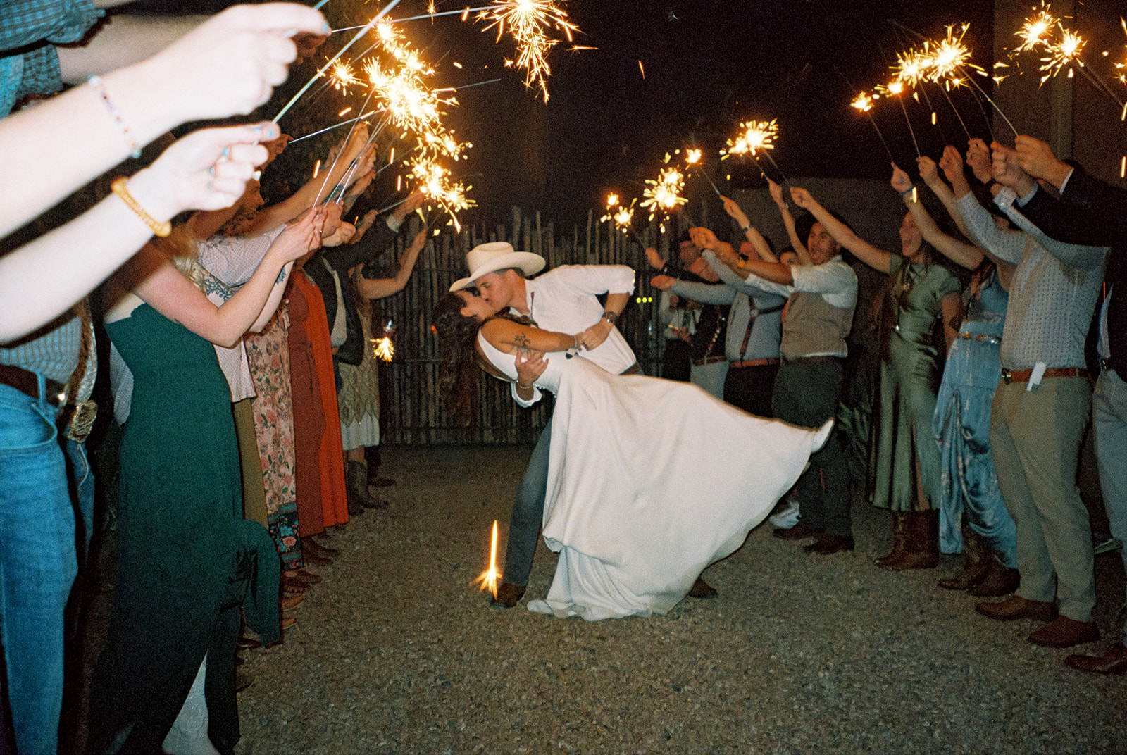 Groom dips bride during grand exit as their guests surround them holding sparklers.