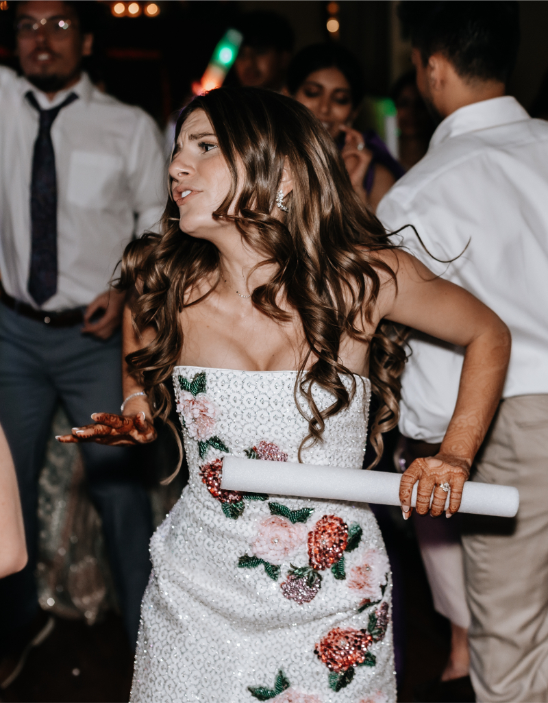 Bride dances energetically with a glow stick, her beaded floral reception dress swaying with movement.